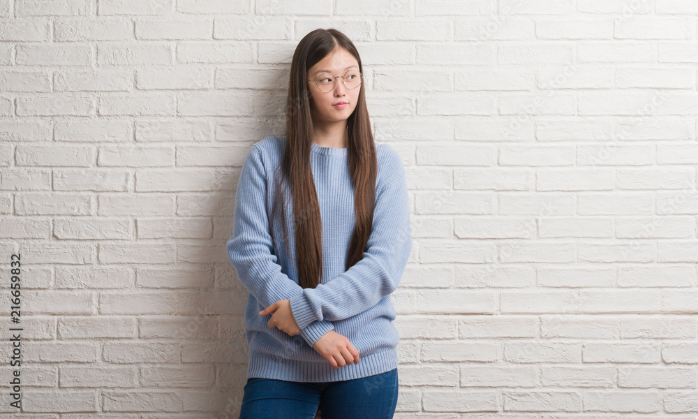 Young Chinise woman over white brick wall smiling looking side and staring away thinking.