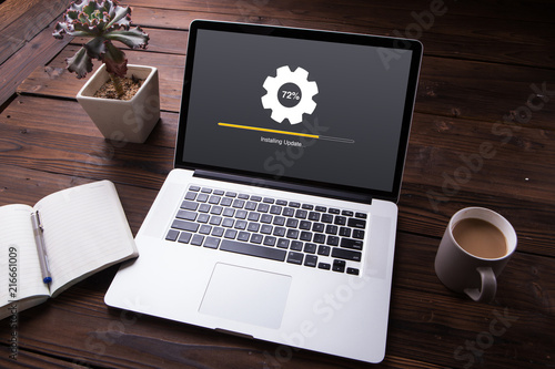 Installing update process with gearbox percentage progress and loading bar on laptop / computer with office equipment on wooden desk background