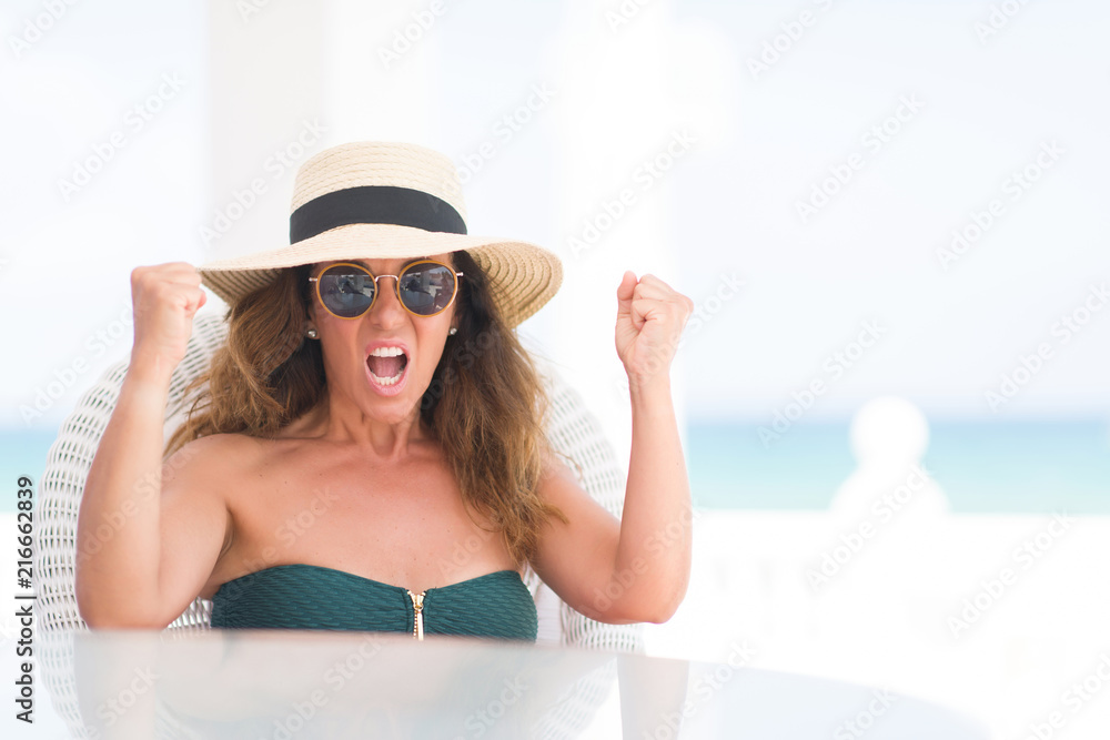 Middle age brunette woman sitting at the table by the beach annoyed and frustrated shouting with anger, crazy and yelling with raised hand, anger concept