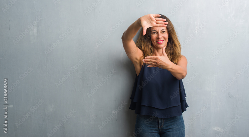 Middle age hispanic woman standing over grey grunge wall smiling making frame with hands and fingers with happy face. Creativity and photography concept. Middle age hispanic woman standing over grey grunge wall smiling making frame with hands and fingers with happy face. Creativity and photography concept.