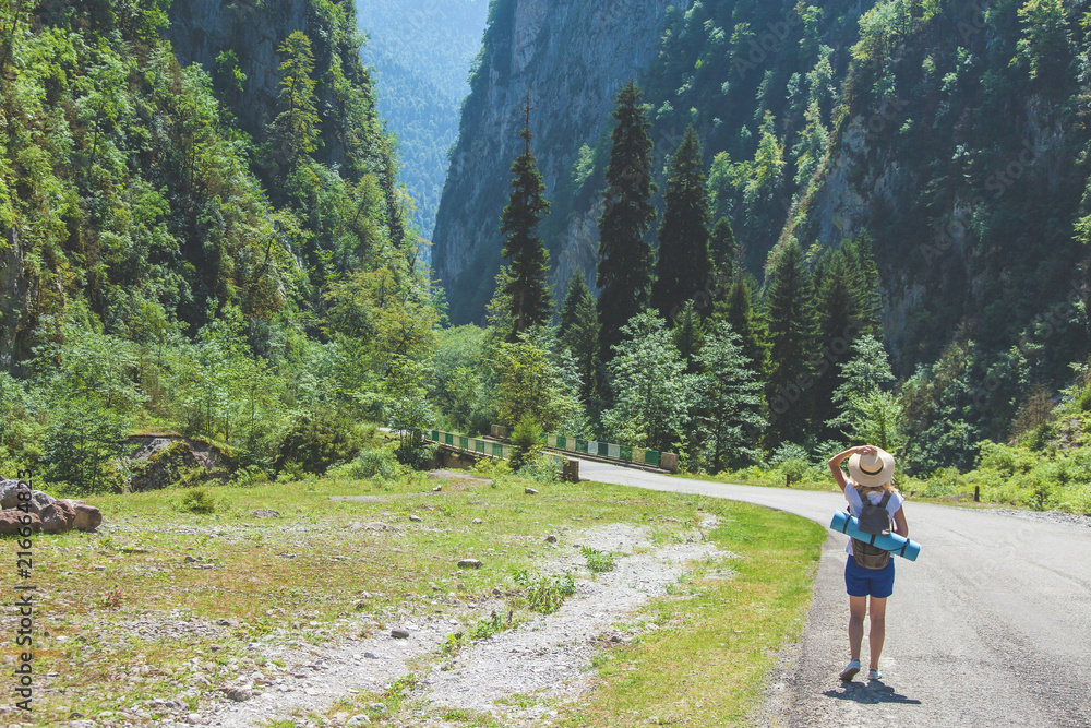 Girl hipster traveler in a hat walking on a road in the background of mountains