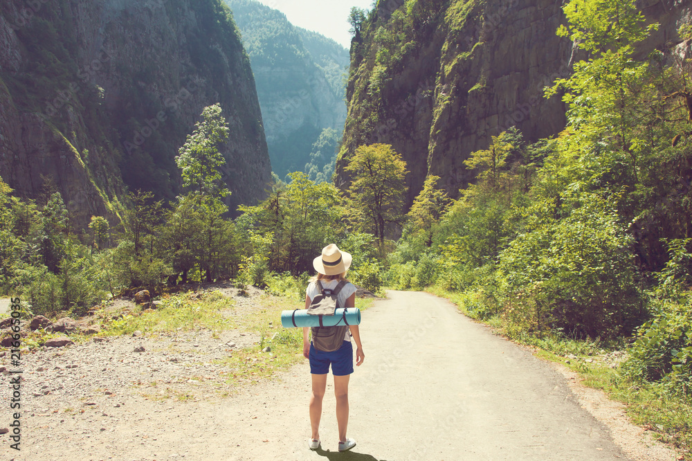 Girl hipster traveler in a hat walking on a road in the background of mountains