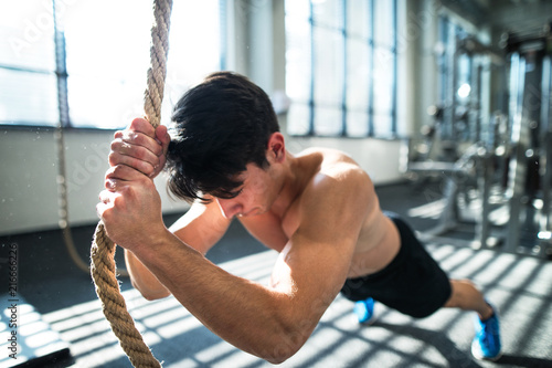 Fit young man in gym working out with climbing rope. photo