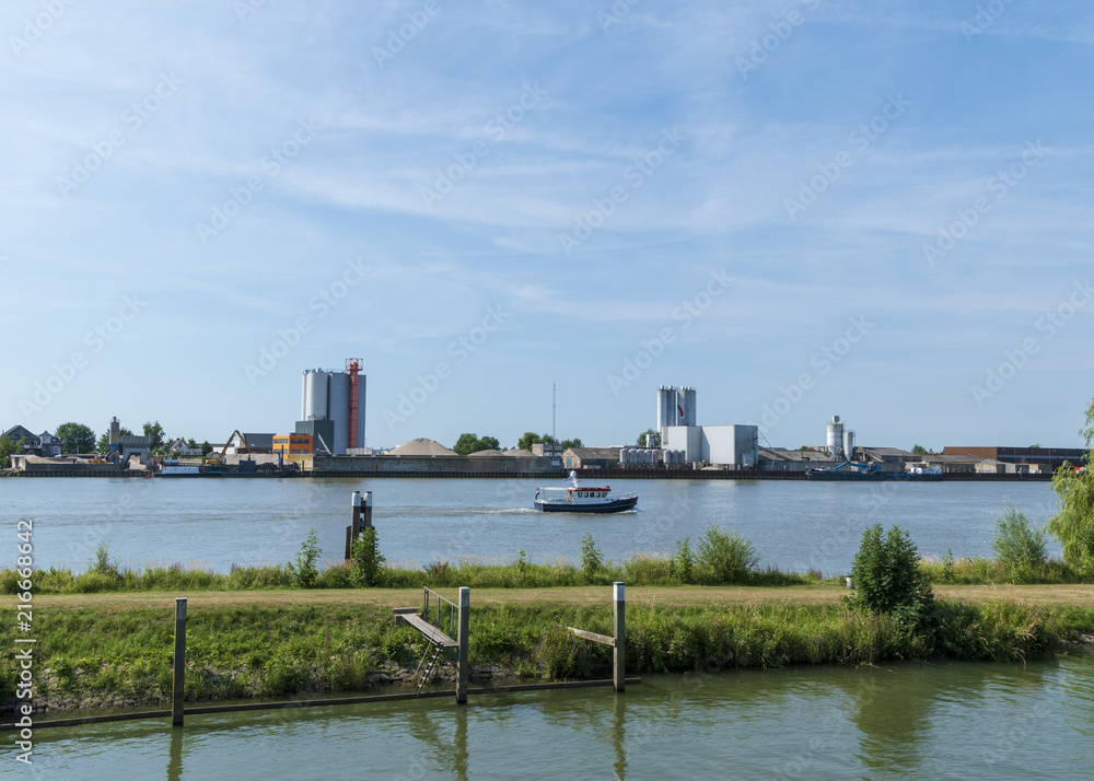 Obraz premium River with factory on the bank and passing boat. Schoonhoven, The Netherlands.