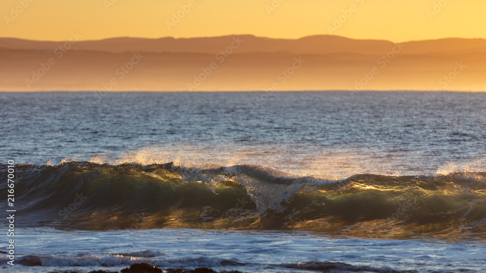 A breaking wave backlit by the rising sun at sunrise giving it a translucent appearance