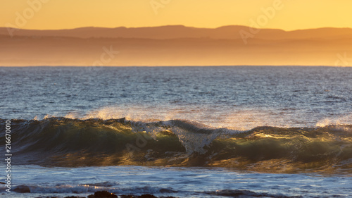 A breaking wave backlit by the rising sun at sunrise giving it a translucent appearance