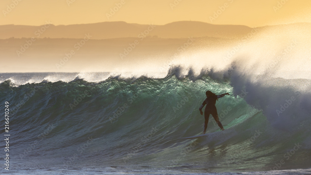 The silhouette of a surfer in a turquoise wave at sunrise