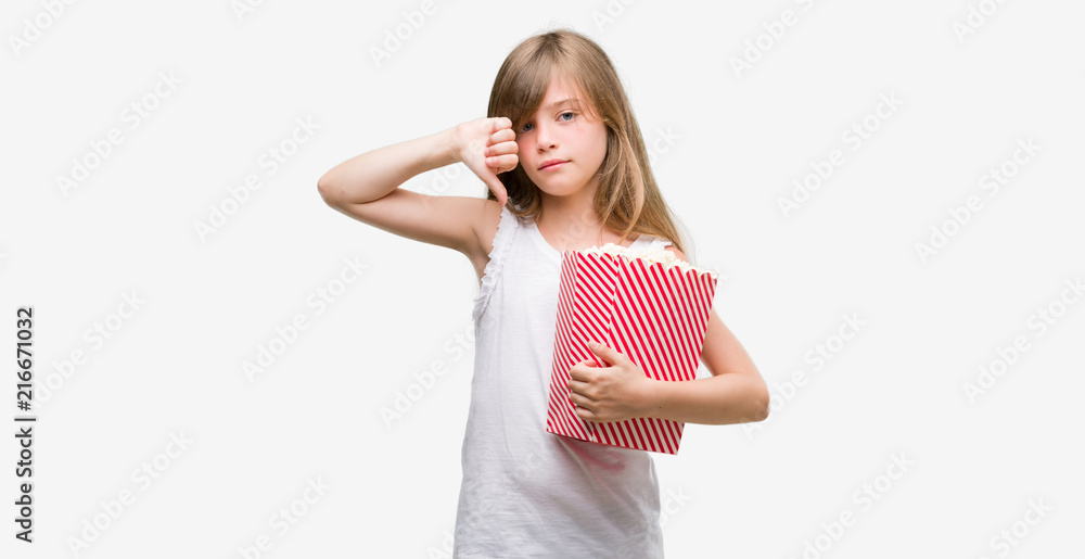 Young blonde toddler holding popcorn pack with angry face, negative sign showing dislike with thumbs down, rejection concept