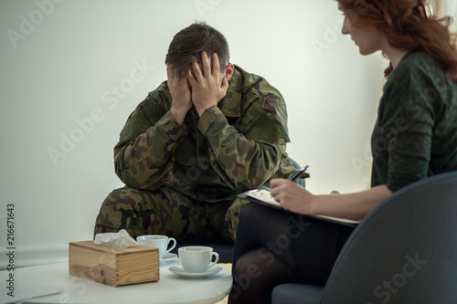 Soldier hiding his face in his hands while talking to a psychiatrist during therapy © Photographee.eu
