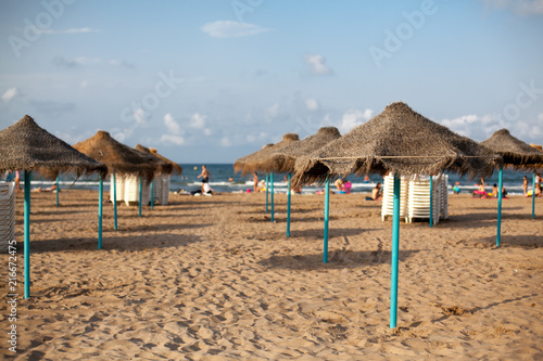 Straw umbrellas on seaside in sunset light. Sand beach in Valencia. Blue sky. Copy space.