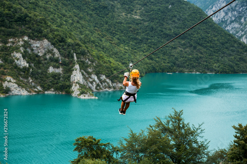 Woman sliding on a zip line over the blue lake