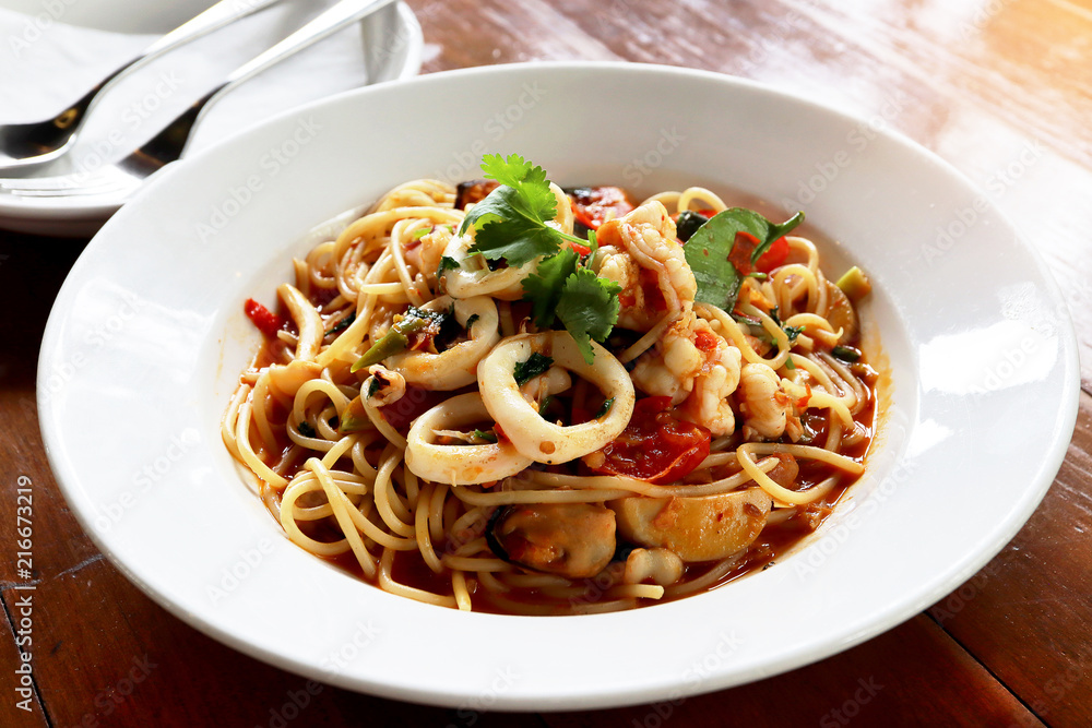 Fresh Spaghetti Spicy Seafood with squid, prawn, mussel, in the white plate on wooden table background. Foods concept.