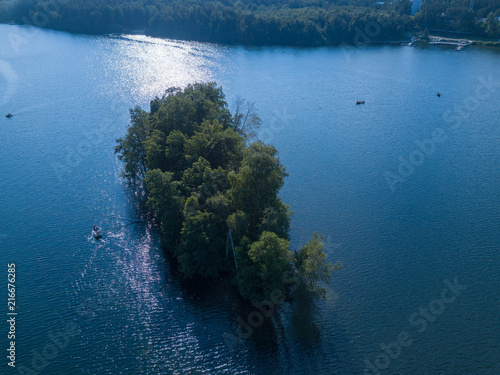 Aerial drone view of piece of forest surrounded by water, mixed forest in the center of lake with floating boats around, Southern Ural - the land of lakes, Russia