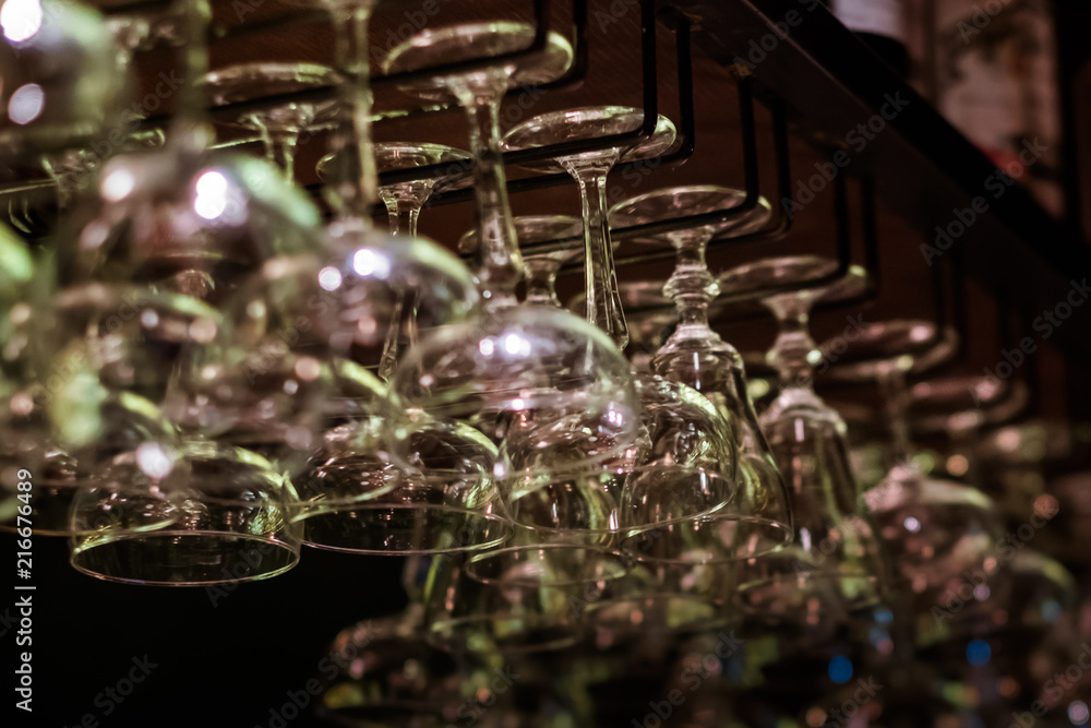 Empty cocktail and wine glasses on bar interior background. Artificial lighting creates reflections and glares in glass. Selective focus in center of image. Empty cocktail and wine glasses on bar interior background. Artificial lighting creates reflections and glares in glass. Selective focus in center of image.