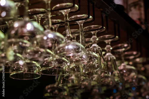 Empty cocktail and wine glasses on bar interior background. Artificial lighting creates reflections and glares in glass. Selective focus in center of image.