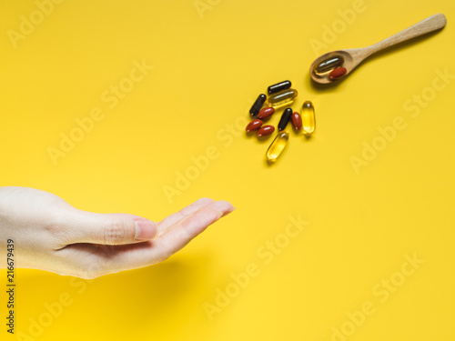 health care and medical concept from minimal flat lay human hand request with soft focus of pill and vitamin in spoon give to with yellow pastel background
