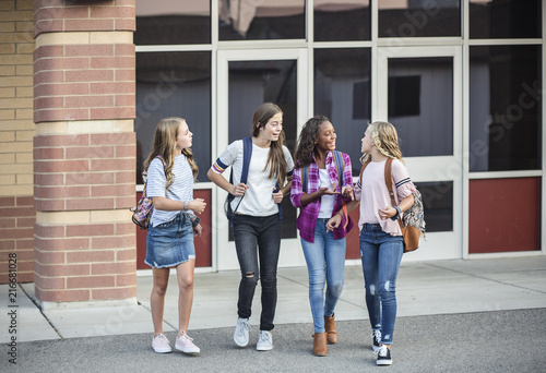 Group of young female friends and students talking together as they leave school for the day