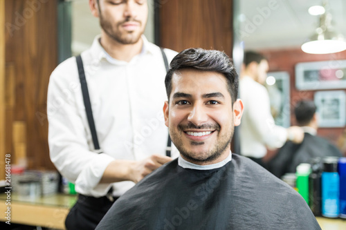 Customer Smiling While Barber Adjusting Hairdressing Cape On Him