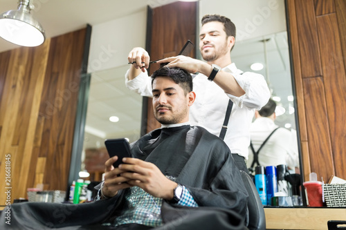 Client Using Smartphone While Hairdresser Giving Him A Haircut