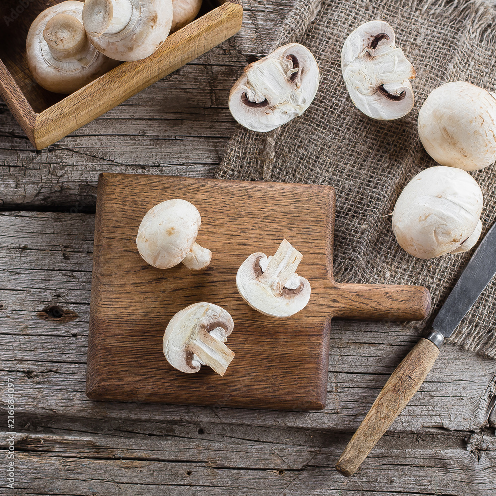 Fresh Raw Mushrooms Champignons on a Wooden Cutting Board on Old Rustic Wooden Table Background Top view