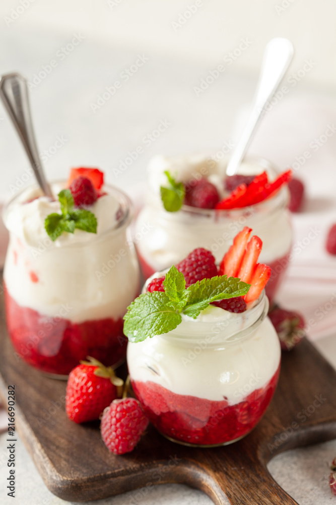 Jars of natural white yogurt with berry sauce decorated with fresh strawberry, raspberry and mint Jars of natural white yogurt with berry sauce decorated with fresh strawberry, raspberry and mint