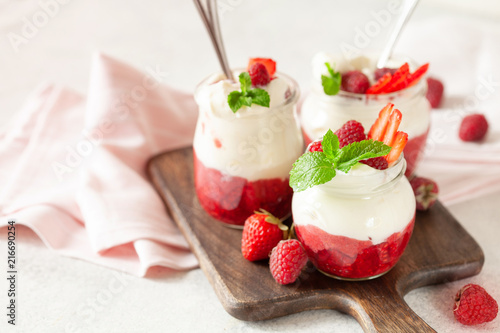 Jars of natural white yogurt with berry sauce decorated with fresh strawbeery, raspberry and mint