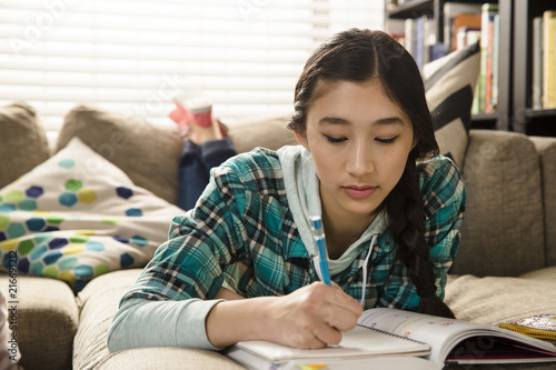 Girl doing homework while lying on couch at home photo