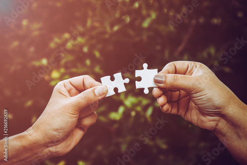 Fotografi two hands trying to connect couple puzzle piece with forest background and light flare; one part of whole; symbol of association and connection for business strategy
