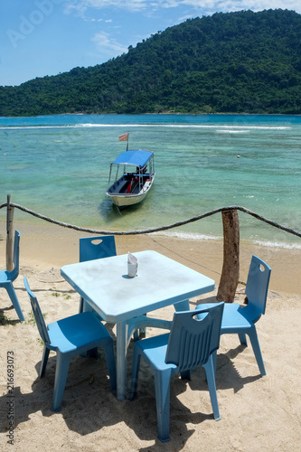 table and four chairs with a boat on a tropical island beach
