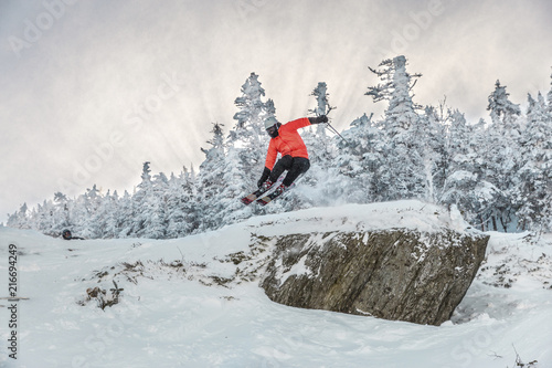 Fotografie Full length of man doing stunt while skiing on snow against trees during winter