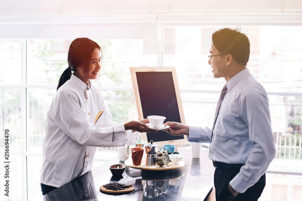 Young Asian female barista making and giving coffee to male customer. Business man receiving coffee at cafe restaurant