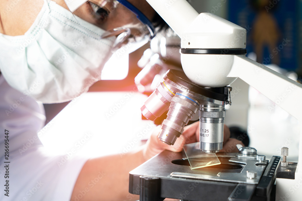 Hands of young Asian man and white microscope in science laboratory with red liquid and dropper for testing. Technician dripping red water on slide glass in science lab. Hands of young Asian man and white microscope in science laboratory with red liquid and dropper for testing. Technician dripping red water on slide glass in science lab.