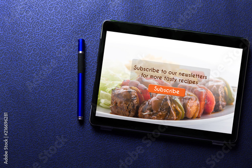 Food blog subscribtion concept on tablet screen with blue pen on blue pattern textured background photo