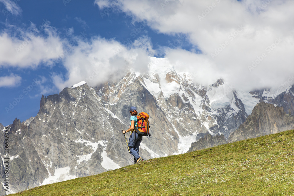 A trekker is walking in front of the Mont Blanc during the Mont Blanc hiking tours (Ferret Valley, Courmayeur, Aosta province, Aosta Valley, Italy, Europe). A trekker is walking in front of the Mont Blanc during the Mont Blanc hiking tours (Ferret Valley, Courmayeur, Aosta province, Aosta Valley, Italy, Europe).