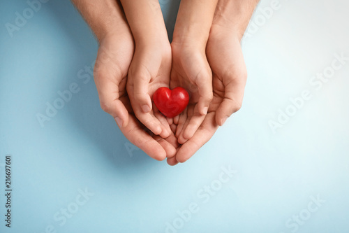 Family holding small red heart in hands on color background