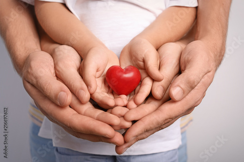 Family holding small red heart in hands together, closeup