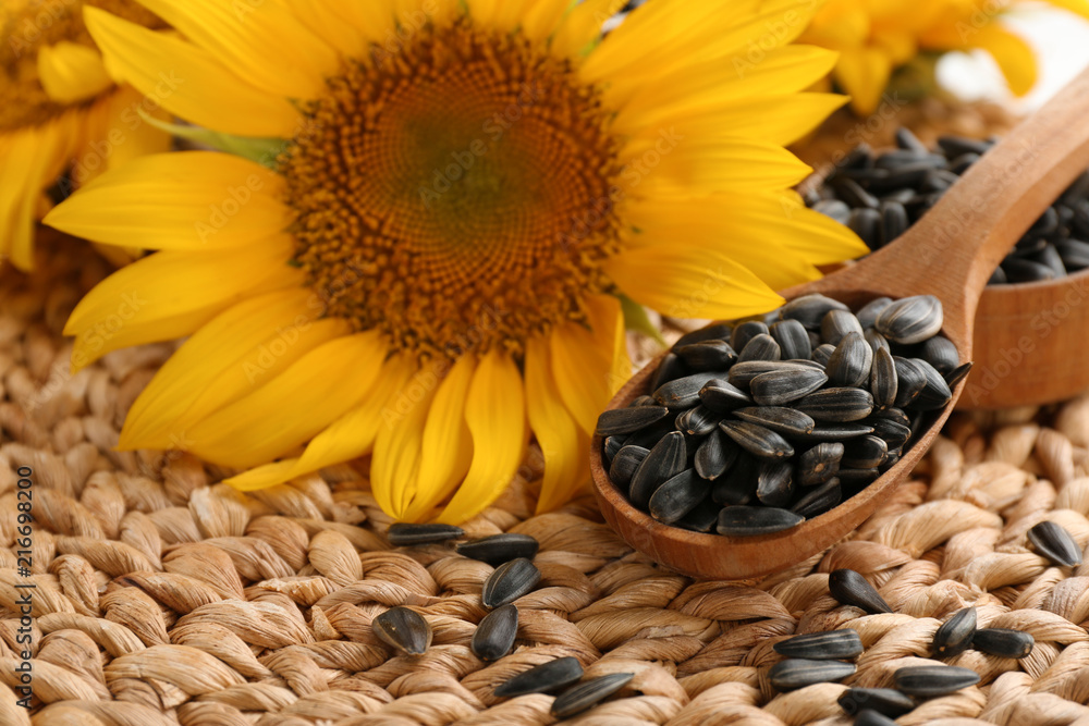 Obraz premium Spoon with sunflower seeds on wicker mat, closeup