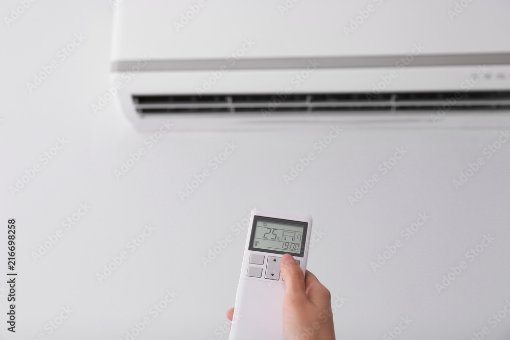 Fototapeta premium Woman operating air conditioner with remote control indoors, focus on hand