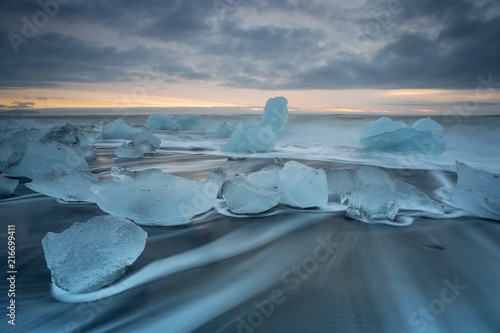 Jokulsarlon beach at sunrise, long exposure photography with waves and pieces of ice on the black sand beach. photo