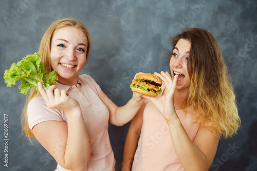 Dieting, difficult choice, healthy vs unhealthy food. Two young women with salad and hamburger. Fighting the temptation