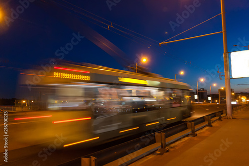 The motion of a blurred trolleybus in the street in the evening.