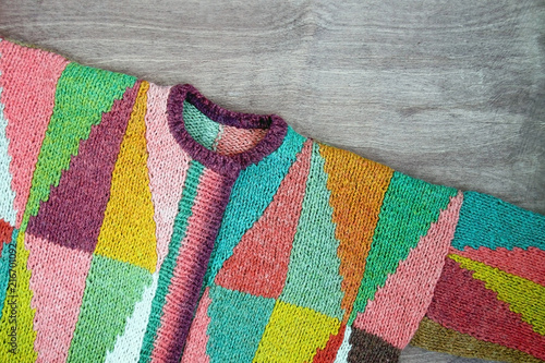 Colorful white, yellow, brown, pink, green, blue, turquoise, orange, claret handmade knitted wool cardigan on the wooden background. Rustic wool.