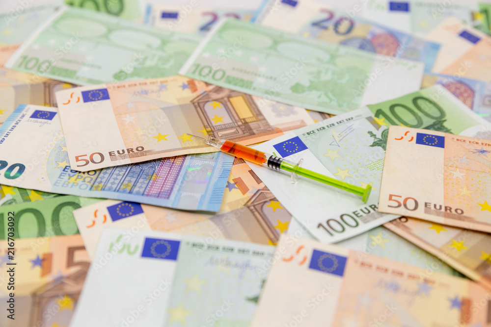 Spread Stack of Euro Banknotes with syringe on top of them, health costs concept Spread Stack of Euro Banknotes with syringe on top of them, health costs concept