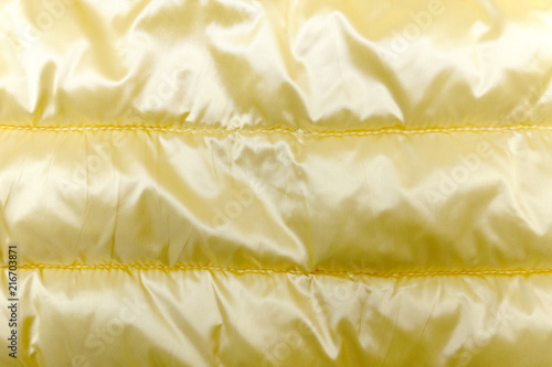 yellow gold duvet covering texture background, silky surface of golden bedding quilt cloth (or winter jacket) with horizontal stitch and creased, close-up top view photo