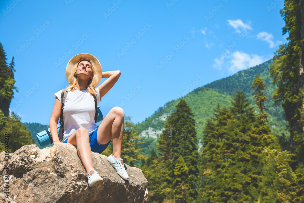 Beautiful Girl Traveler sits on a mountain and enjoys the sun on a background of mountains Beautiful Girl Traveler sits on a mountain and enjoys the sun on a background of mountains