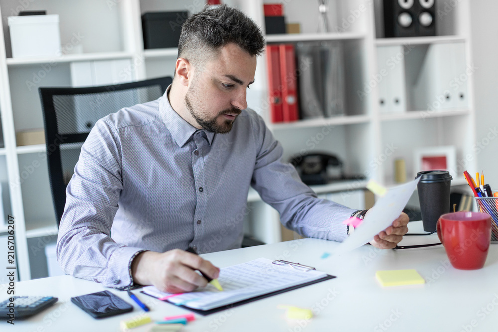 A young man in the office sits at a table, holds a marker in his hand and works with documents. A young man in the office sits at a table, holds a marker in his hand and works with documents.