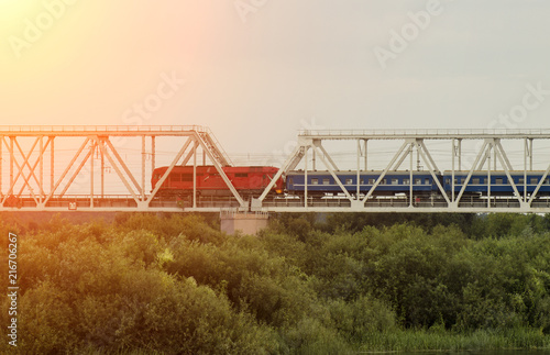 Passenger train rides along the railway bridge over the river, the sun © HENADZY