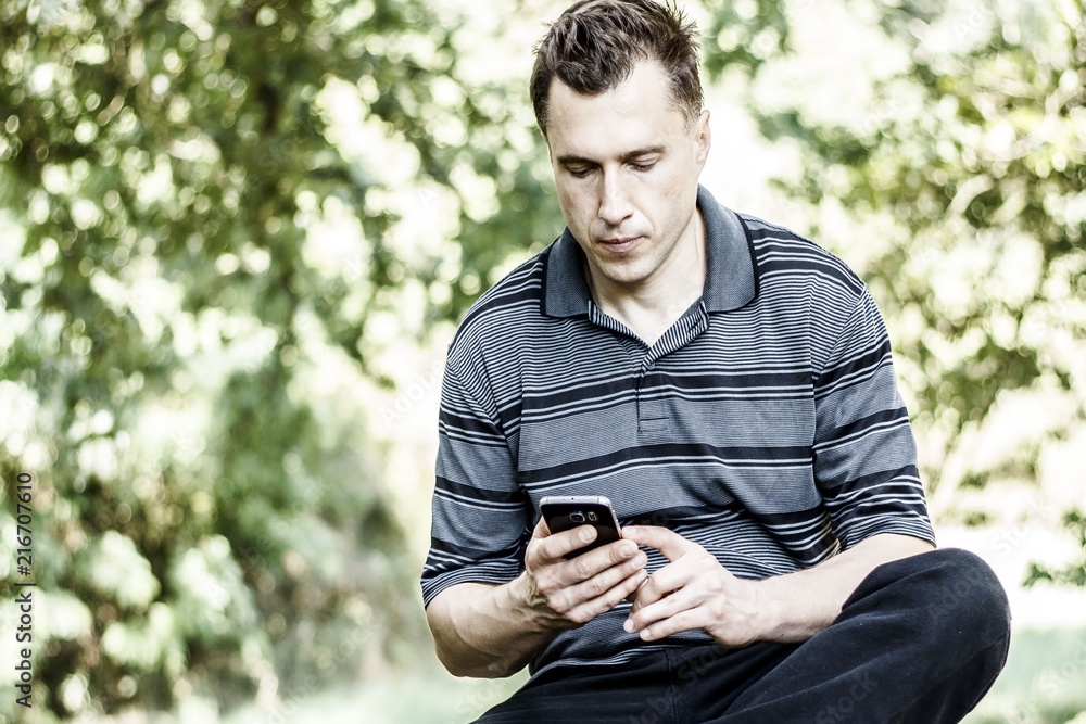 Young man texting on the phone in the park Young man texting on the phone in the park