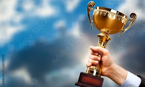 Hand holding golden trophy on sky background