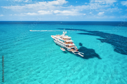 Yacht on the azure seashore in balearic islands. Aerial view of floating boat with people in transparent sea at sunny day in summer. Top view from drone. Seascape with luxury yachts in motion in bay © den-belitsky